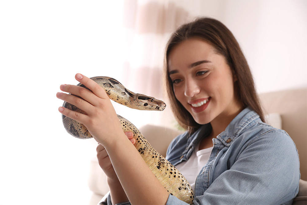 A smiling woman holding her snake in her arms.